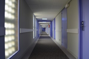 Dark gloomy, sparse hotel hallway with purple room doors.